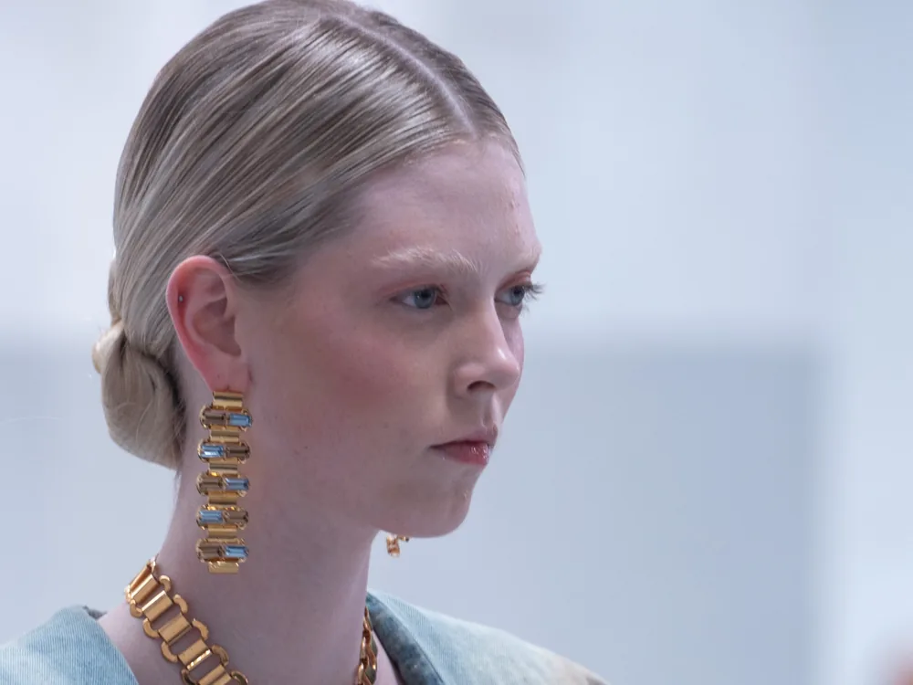 Una modelo rubia en la pasarela, con recogido bajo, collar dorado y el rostro apenas maquillado