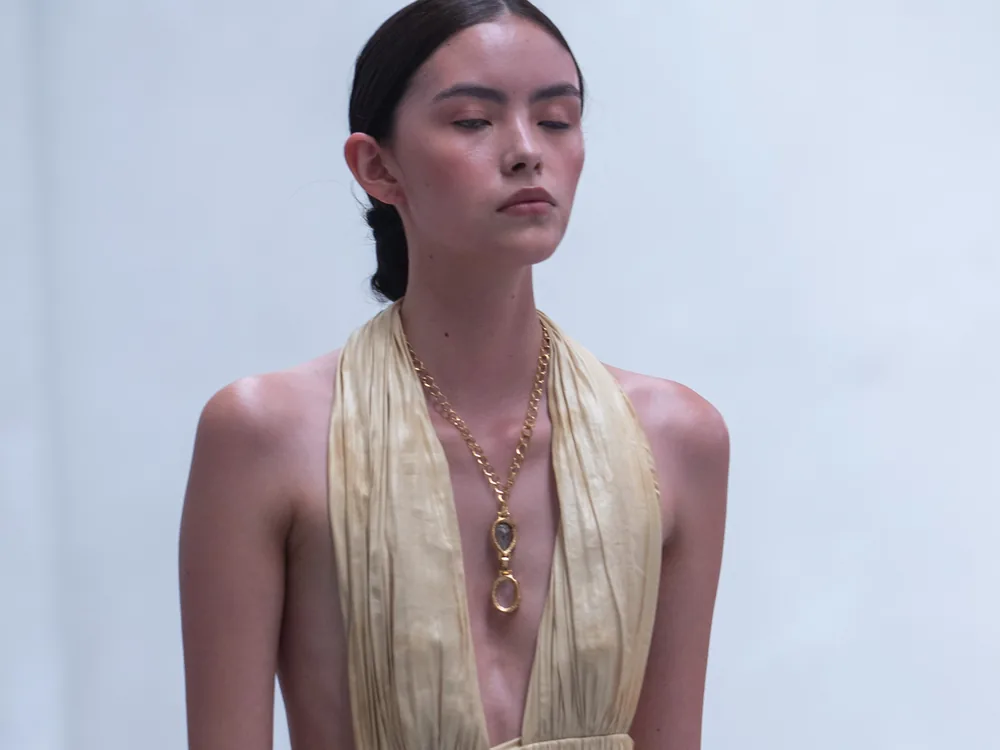 Una modelo con vestido halter dorado, los ojos cerrados y la piel con brillo