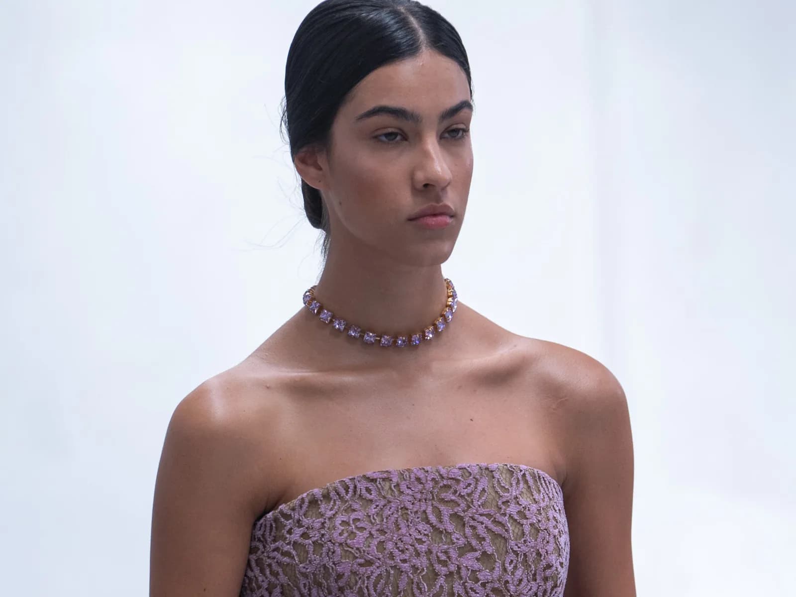 Una modelo en la pasarela con vestido palabra de honor malva y gargantilla, la piel natural y luminosa