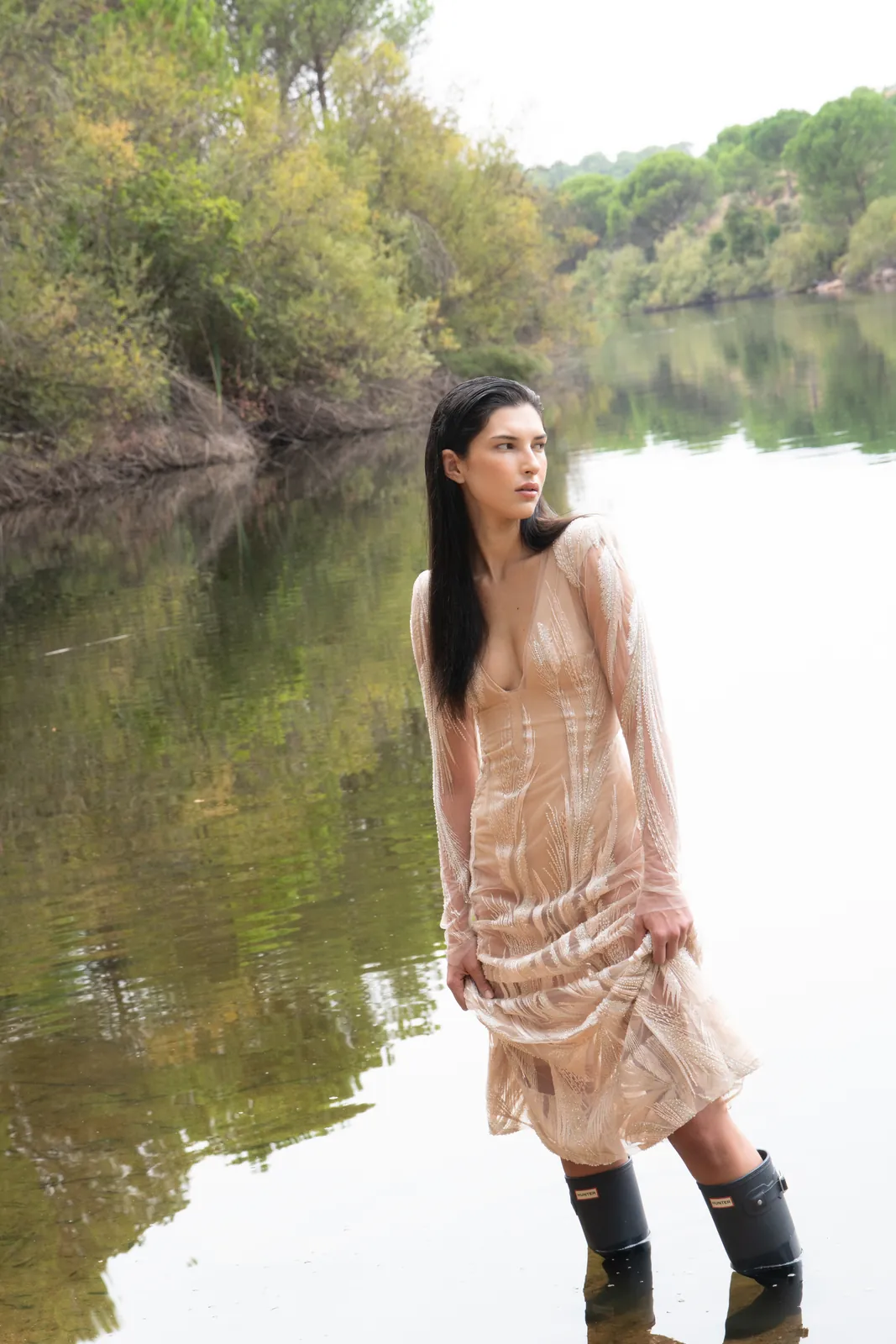 Bruma: vestido nude bordado y botas de agua, con los pies dentro del embalse